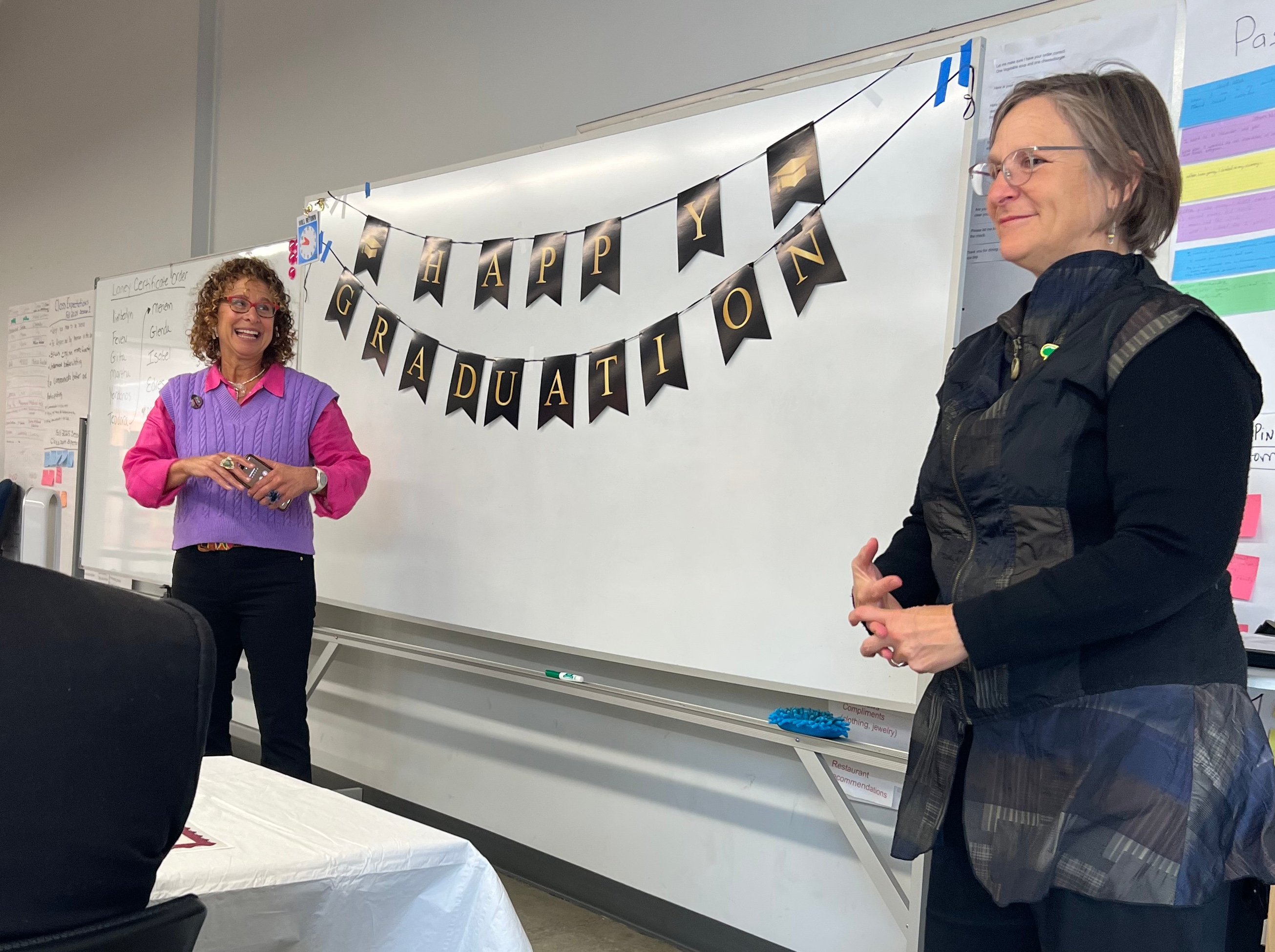 Two Laney College employees address the audience at the Vocational English as a Second Language graduation December 2025