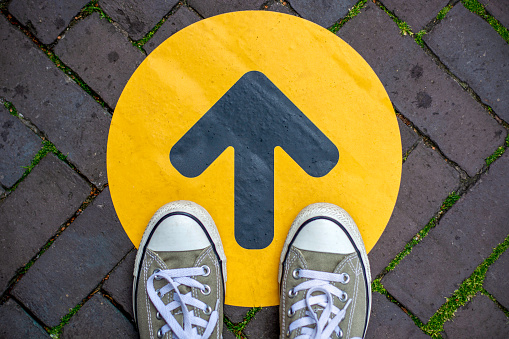 sneakers from above standing on a yellow arrow pointing forward